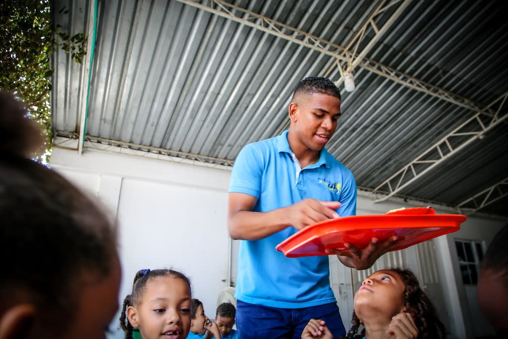 Francisco wears a blue shirt and carries a red tray to serve food at his former Compassion centre.
