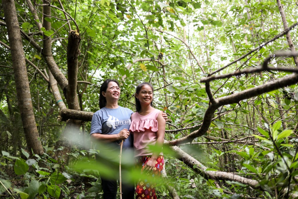 Two women stand in a forest.
