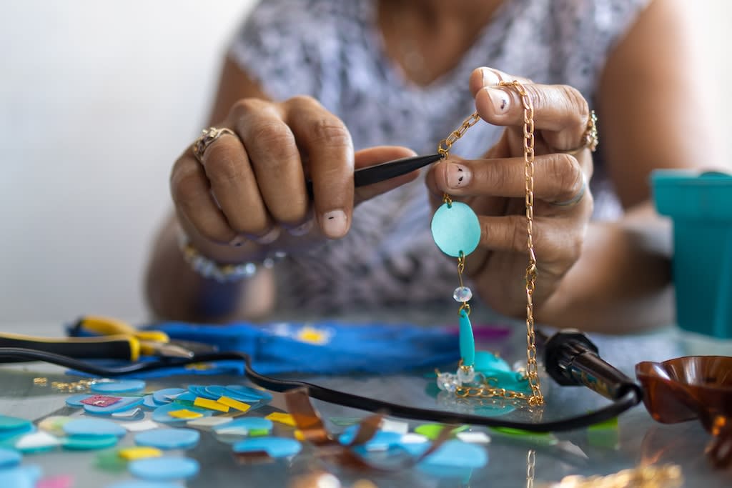 A close-up of hands making recycled jewelry with blue beads made from recycled bottles.