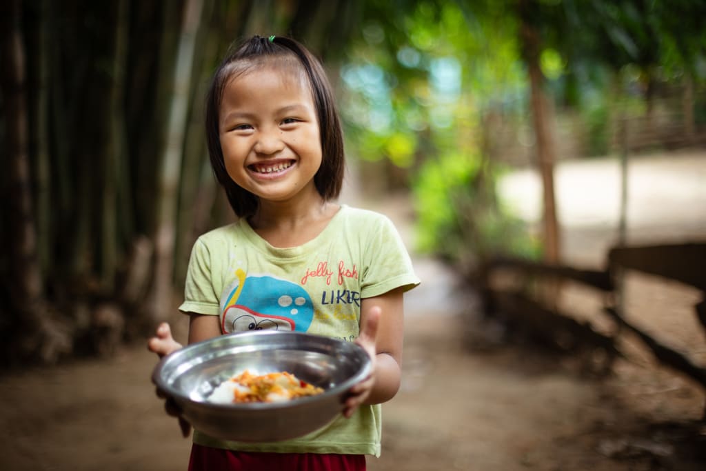A girl in a pale green t-shirt holds a plate full of food and smiles.