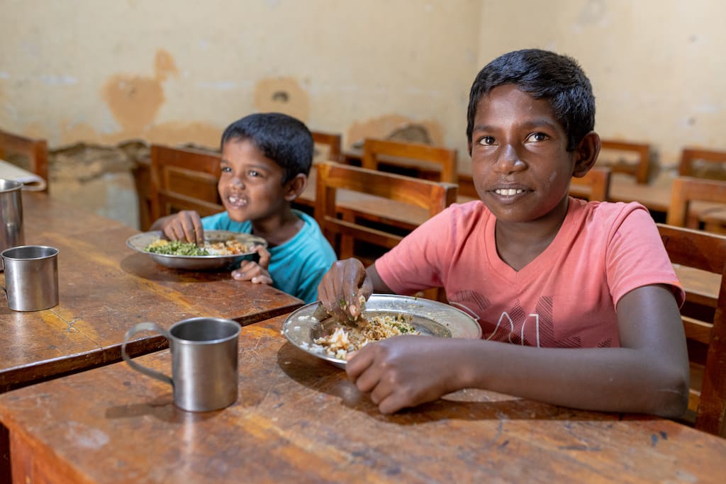 Two boys in Sri Lanka sit at a table eating a meal.