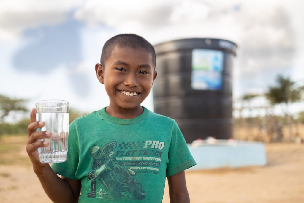 A boy in Colombia holds up a clean glass of water. Access to Clean Water is a gift in the Gifts of Compassion gift guide.