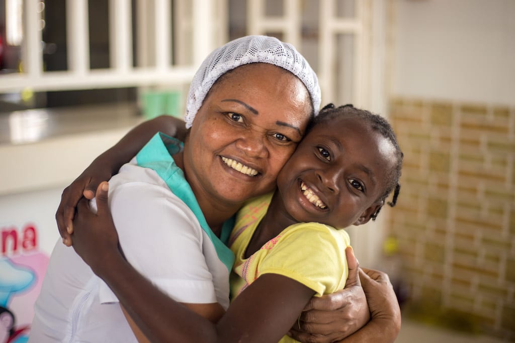 Woman with a hairnet hugs a child from the centre while smiling.