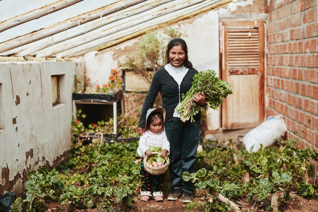 A mother and daughter standing in a garden holding vegetables.