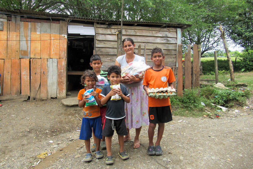 A family in Colombia stands outside their home with groceries provided by Compassion.