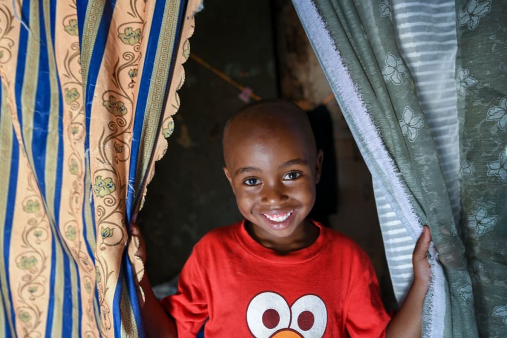A boy in a red shirt smiles between two curtains
