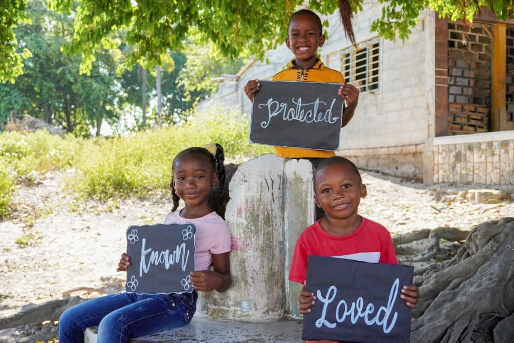 Three children hold signs that read Known, Loved and Protected