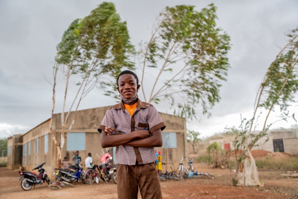 Sansan, a young boy from Burkina Faso stands smiling, arms crossed