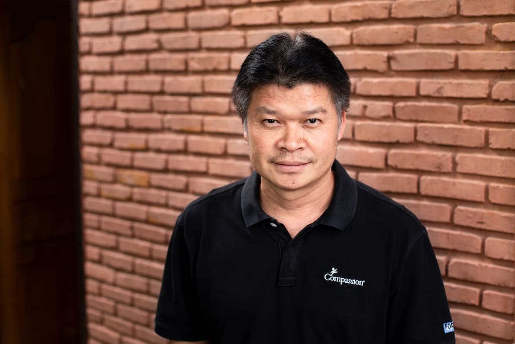 Surachai, Compassion Thailand's Manager of Partnership, is wearing a black shirt and is standing in front of a brick wall.