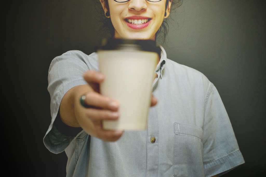 A girl wearing a denim shirt gives a coffee to the camera