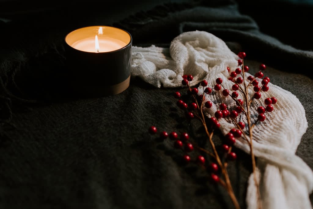 A candle sits beside a white scarf and a cranberry plant