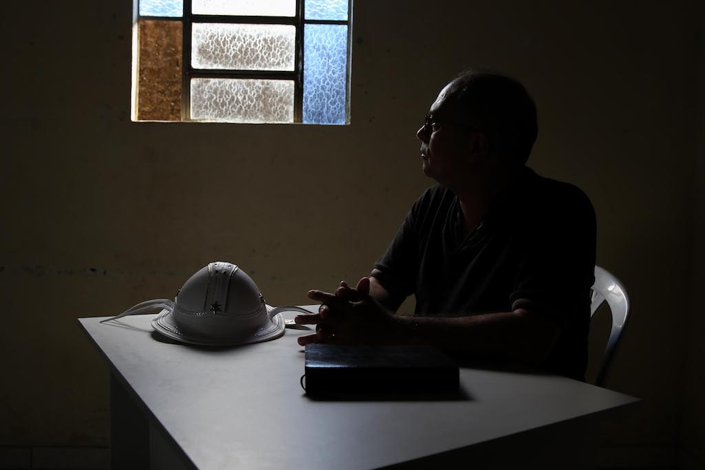 A silhouette of Pastor Linaldo, sitting at a table inside his church building.