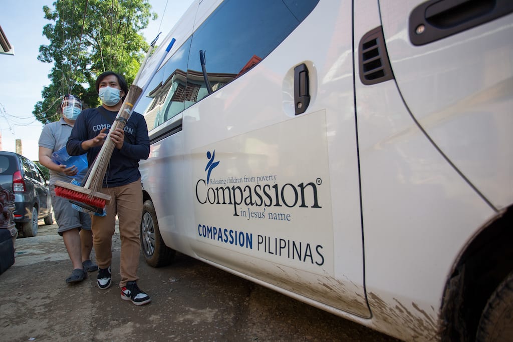 Two men in face masks beside a van with the Compassion logo on the side.
