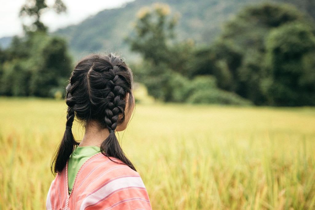 A silhouette of a Thai girl wearing a pink poncho and two braids.