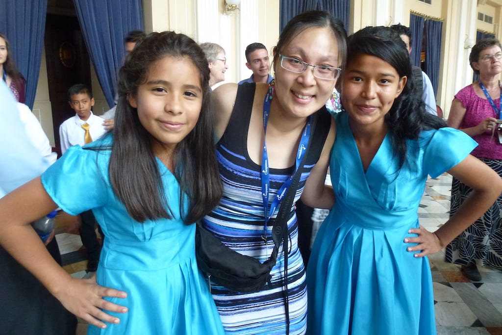 Andrea poses with two girls in El Salvador, they are all wearing blue dresses.