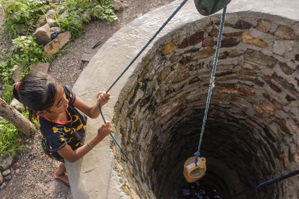 An overhead photo of Yunita collecting water from the old well.