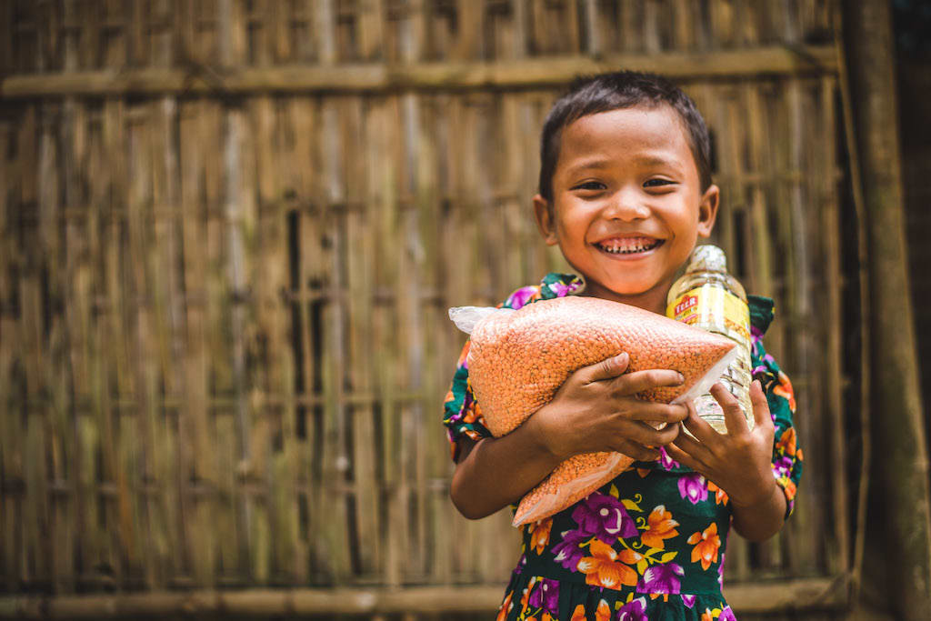 A young Bangladeshi child carrying an armful of groceries delivered by Compassion staff.