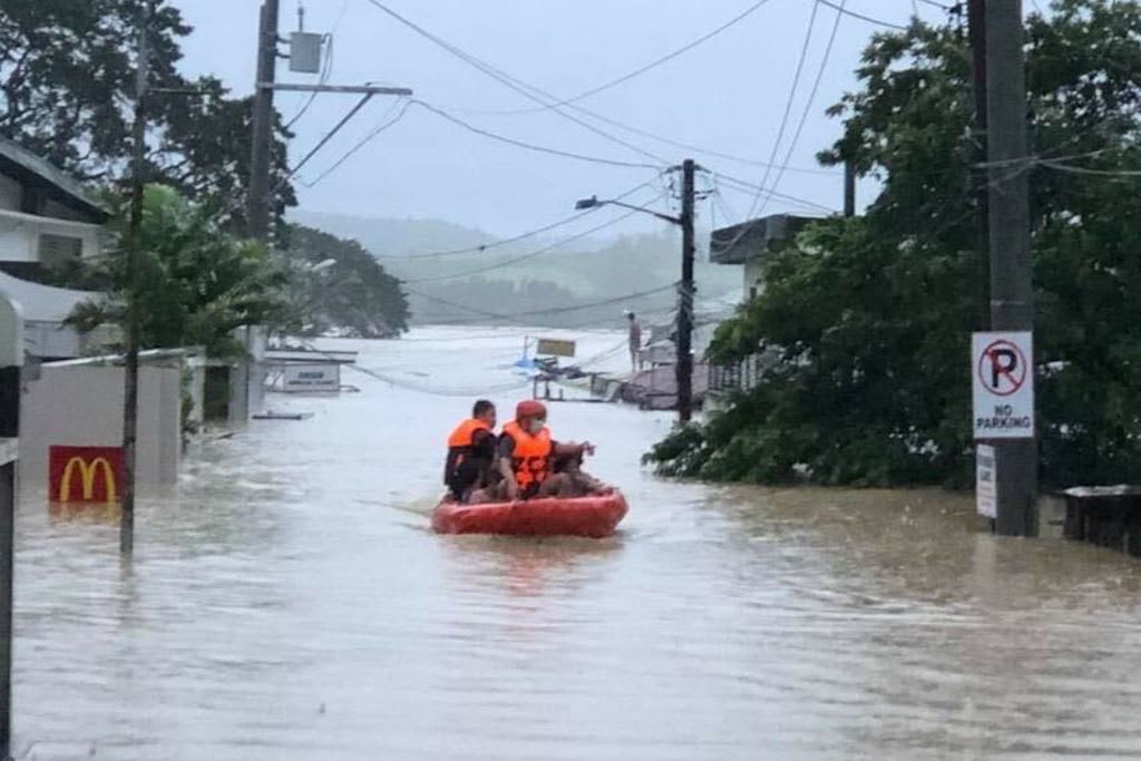A small raft with several rescue team members on board floats through a flooded street.