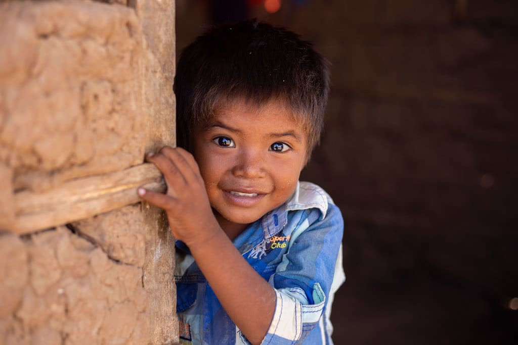 A little boy wearng a blue shirt peaks out of a wall smiling