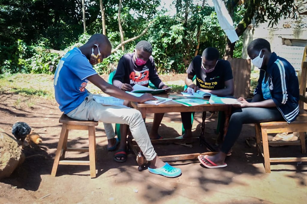 A group of Compassion-sponsored students study together outside at their Compassion centre. They are sitting at a table and all wearing cloth protective face masks.