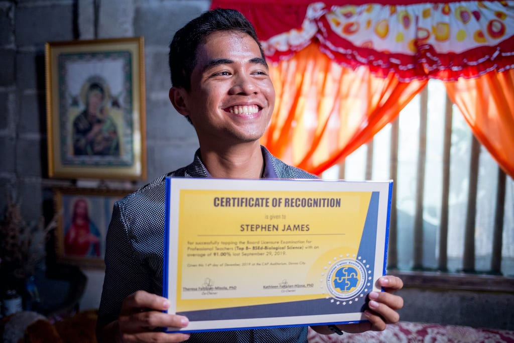 Stephen sits in his home, smiling and holding up a certificate of recognition.
