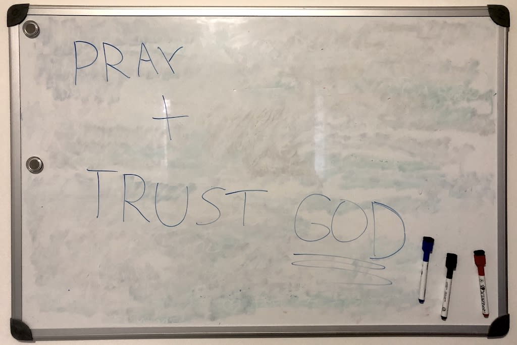 A whiteboard with the words "Pray and trust God" written on it.