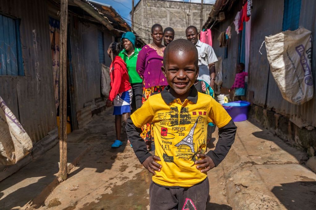Livingstone stands in the foreground with his hands on his hips, wearing a yellow shirt. His family stands in the background behind him.