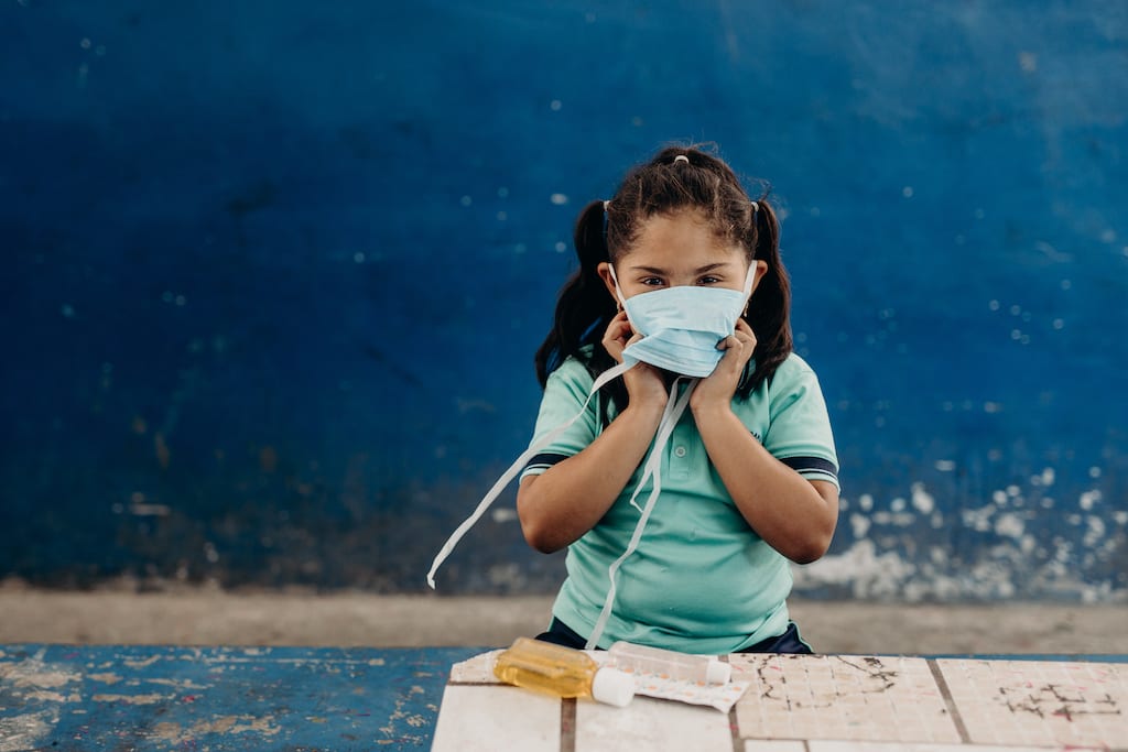 A Salvadoran girl holds a face mask to her face.