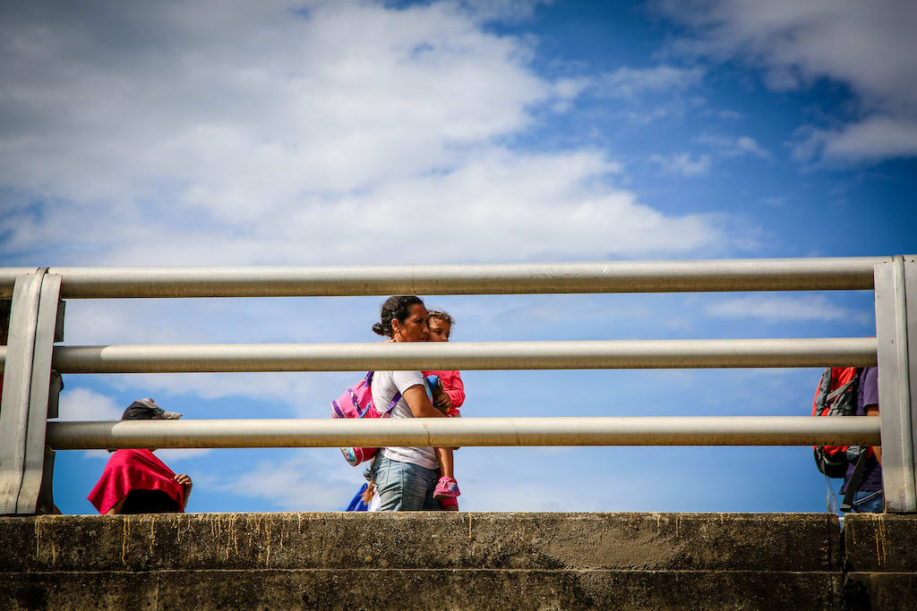 A woman carrying a toddler crosses a bridge at the Venezuela-Colombia border.