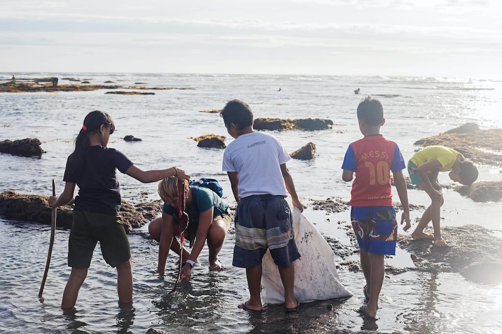 Four kids hold garbage bags while wading into the shore of a beach.