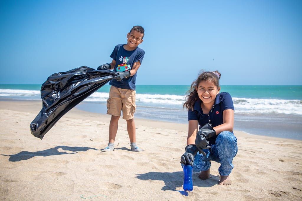 A young boy and girl pick up garbage from the beach.