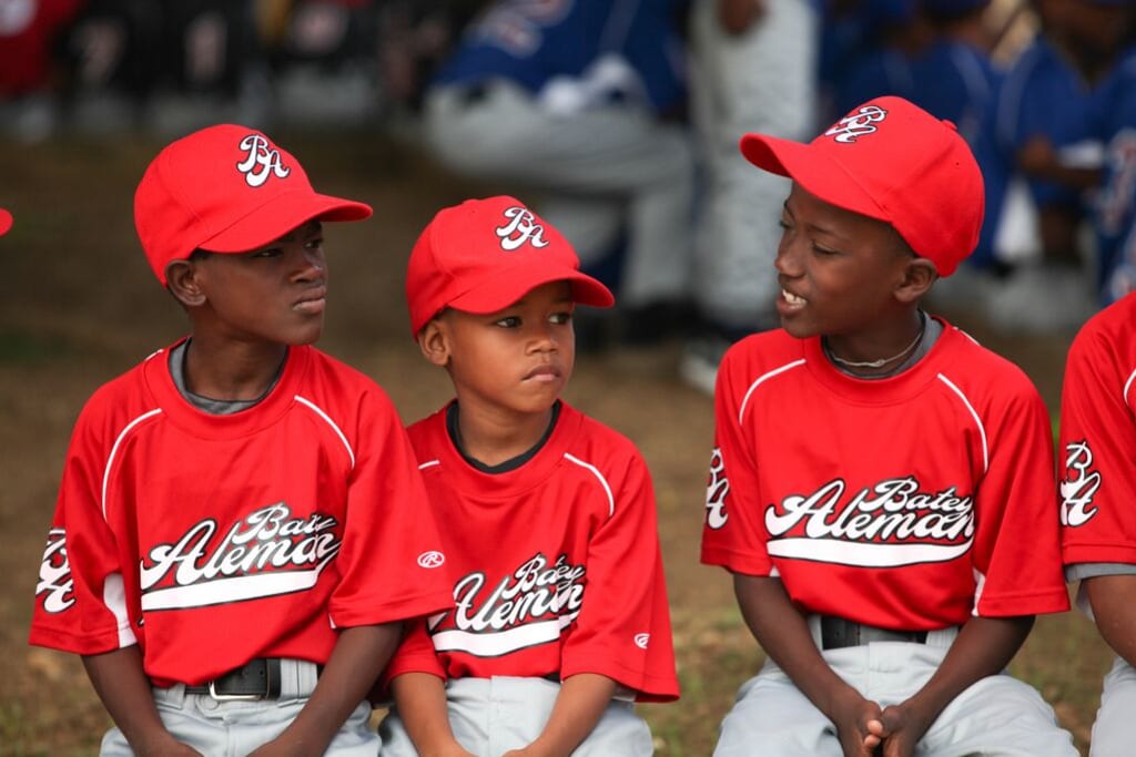 Three kids wearing a red uniform wait at the sidelines