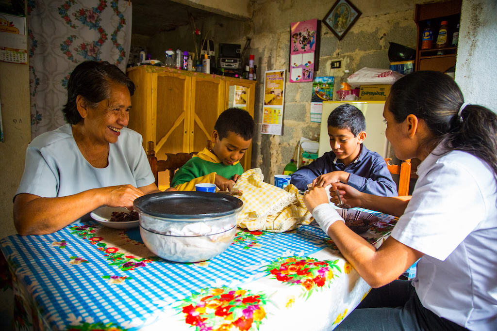 Hector, his brother, aunt and grandmother sit around table in their home eating a meal together.