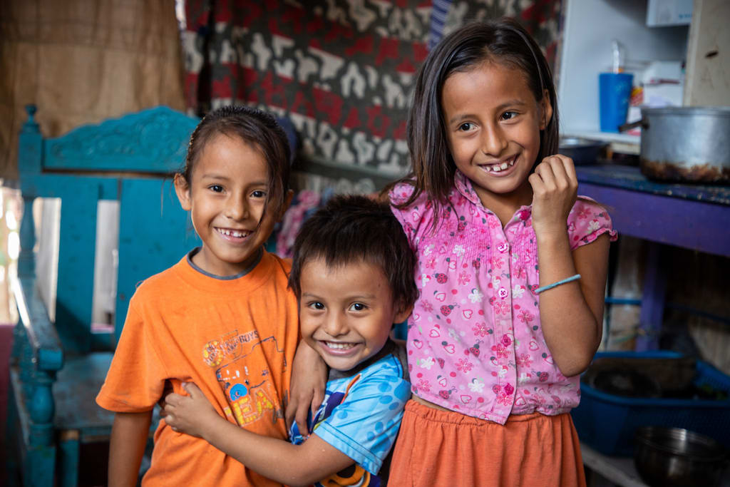 Three Ecuadorian children laughing and hugging each other.