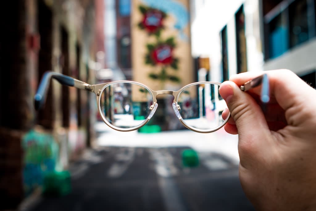 A hand holding out a pair of glasses looking into an alley.