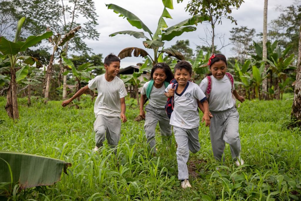 A group of found children run in a field, on their way to school.