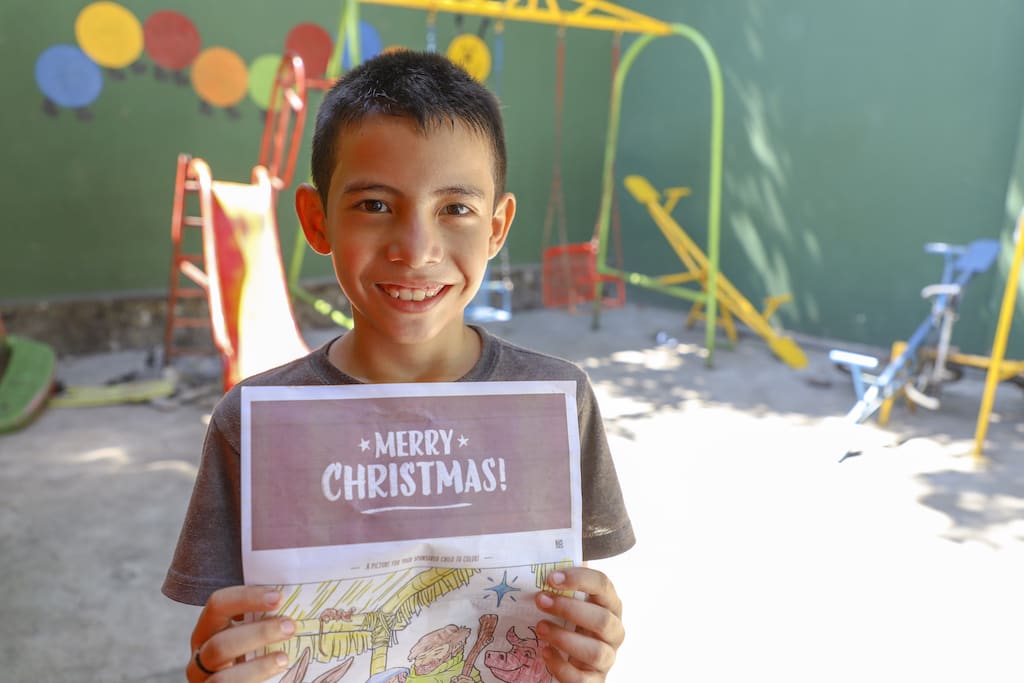 A boy holds up a letter with the heading 'Merry Christmas!'