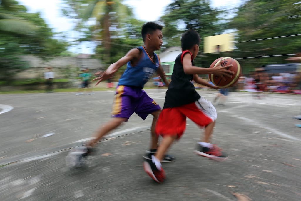 Two boys on opposite teams playing basketball. One boy is dribbling while the other defends.