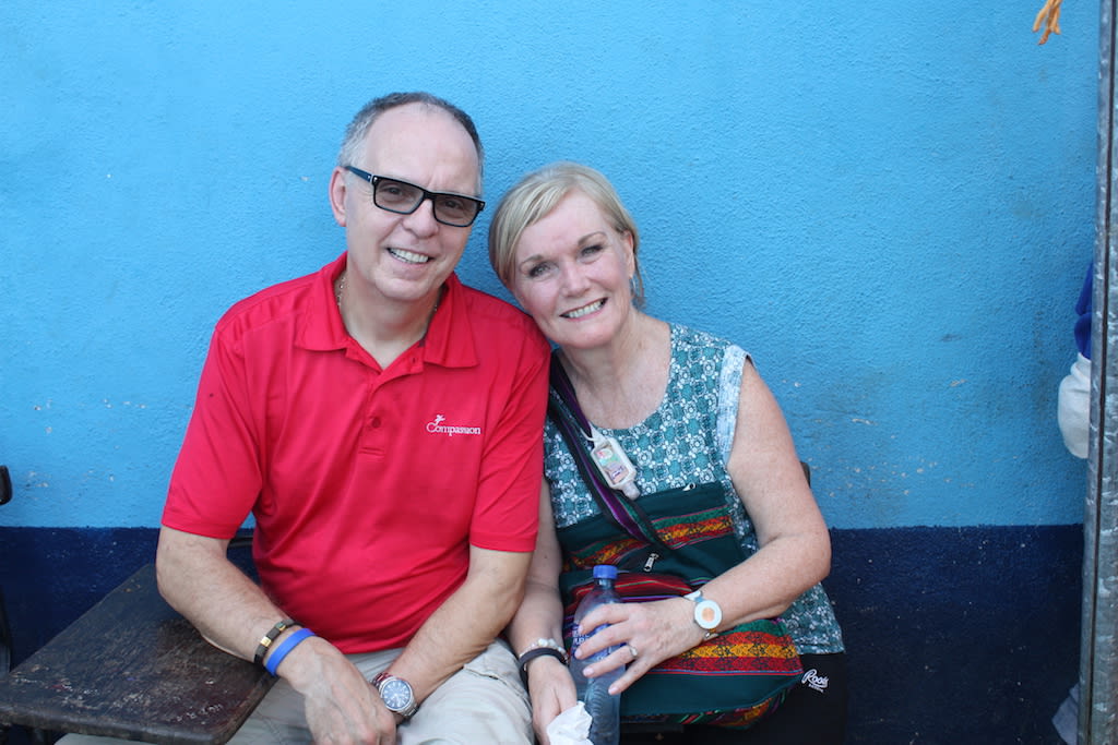Barry and Sharon together in one of Compassion's field countries. Barry is wearing a read polo shirt and Sharon is wearing a blue patterned top.