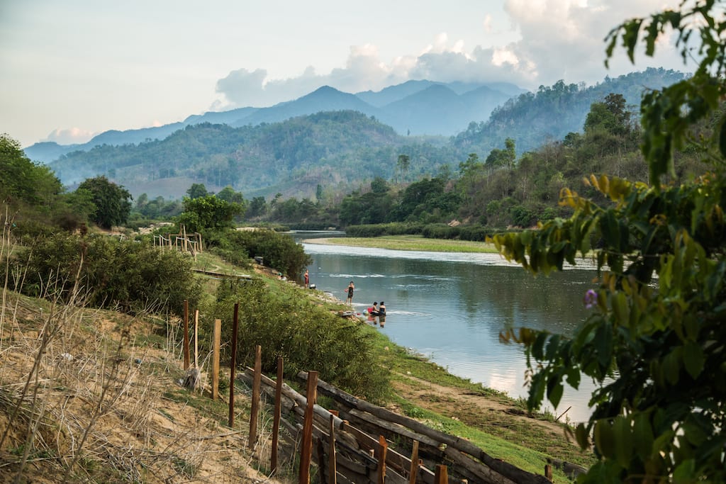 A landscape in rural Myanmar. There is a river in the foreground and green mountains behind.