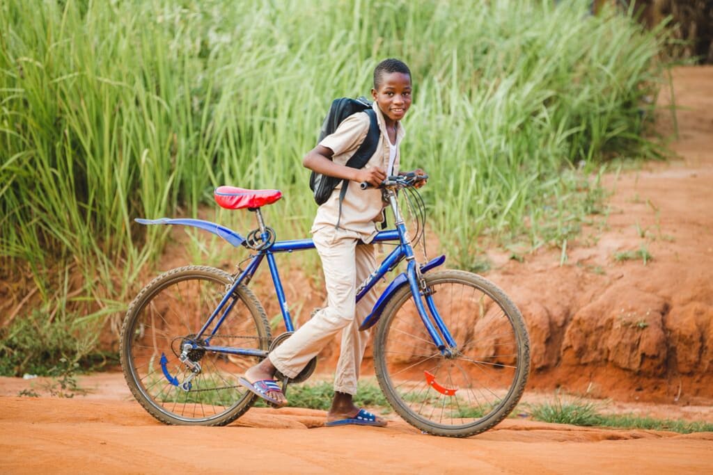 little boy wearing a black backpack and a blue bike on a dusty red road