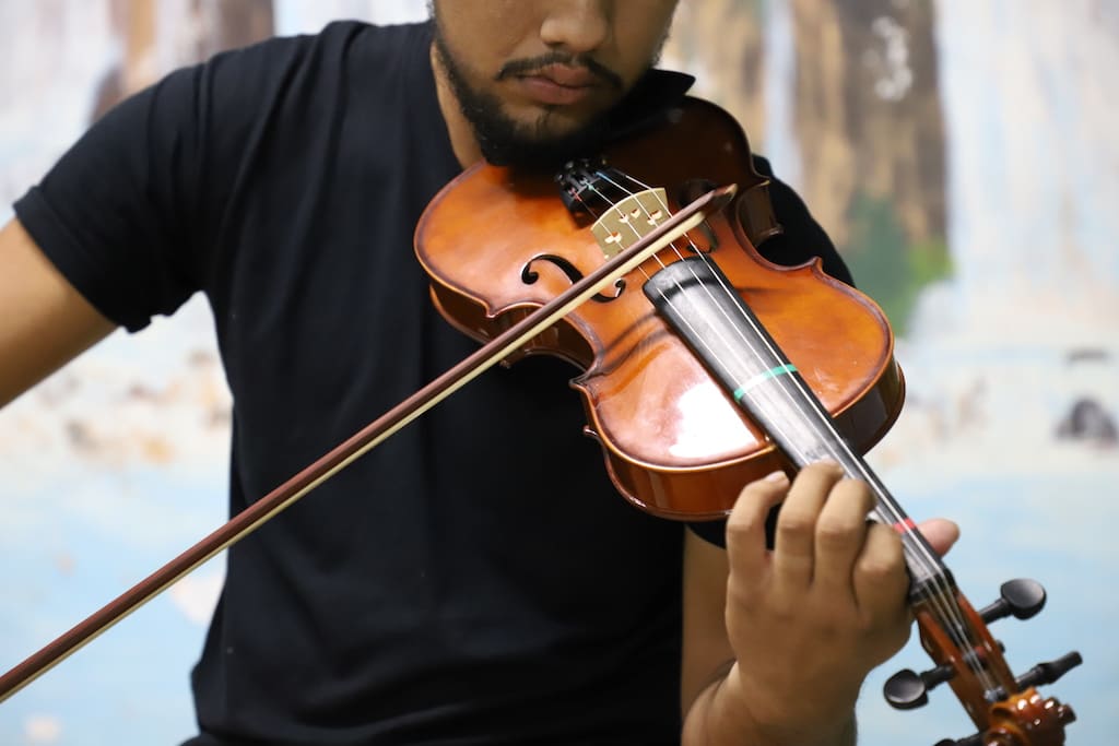 A man wearing a black t shirt is playing the violin. It is a closeup, without showing his eyes.