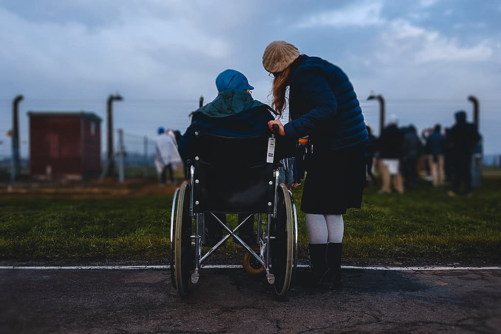 A woman stands beside another woman who is using a wheelchair.