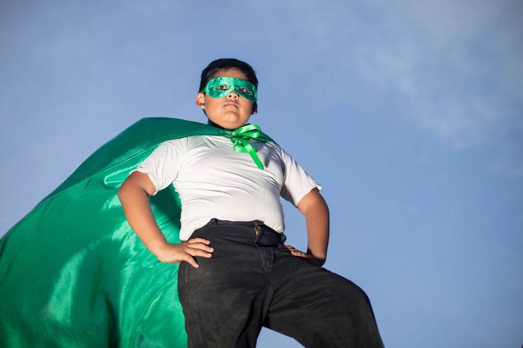 Rafael is wearing a white shirt, black jeans, and a green cape. He is standing outside.