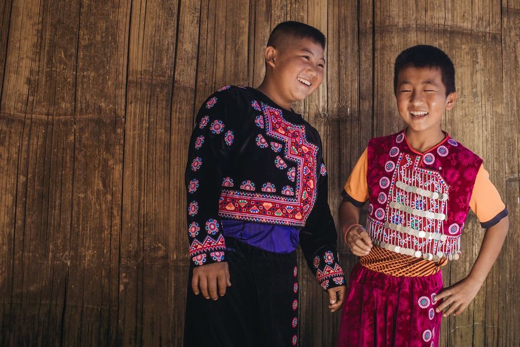 Two boys standing at the Compassion centre wearing their Hmong traditional dress, laughing with each other.