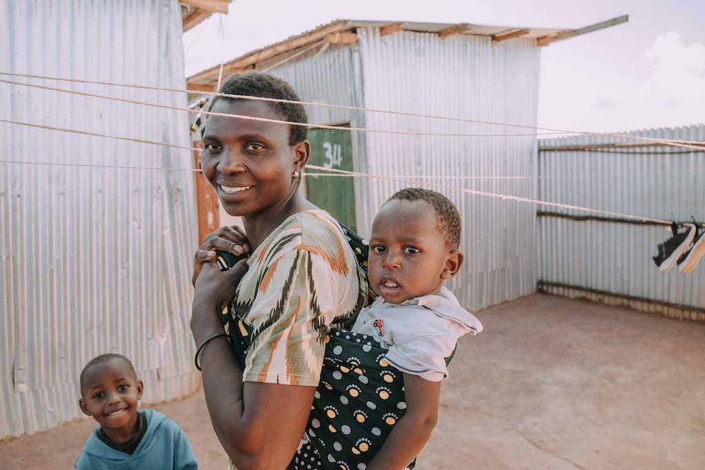 Franciska smiles at the camera with her baby on her back and other son standing beside her smiling.