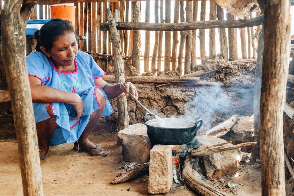 Woman crouches by a fire making food over a pot.