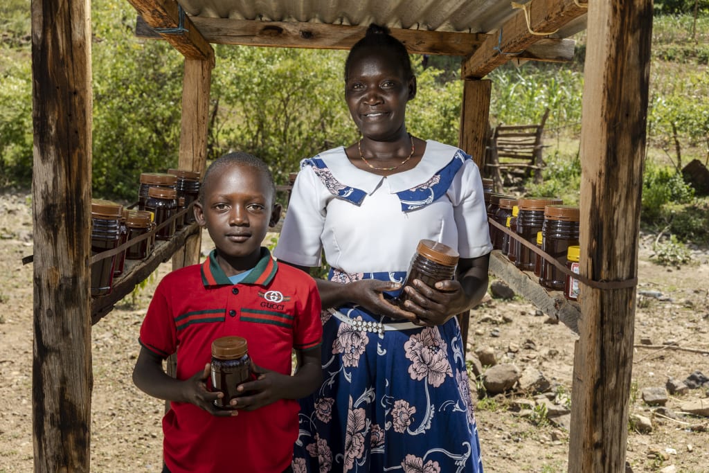 A mother and son hold honey from the beekeeping income generation initiative.