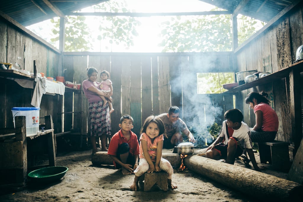 A family in their home cooking dinner. The kids smile at the camera. Their father was a carpenter and was in an accident that plunged his whole family into poverty.