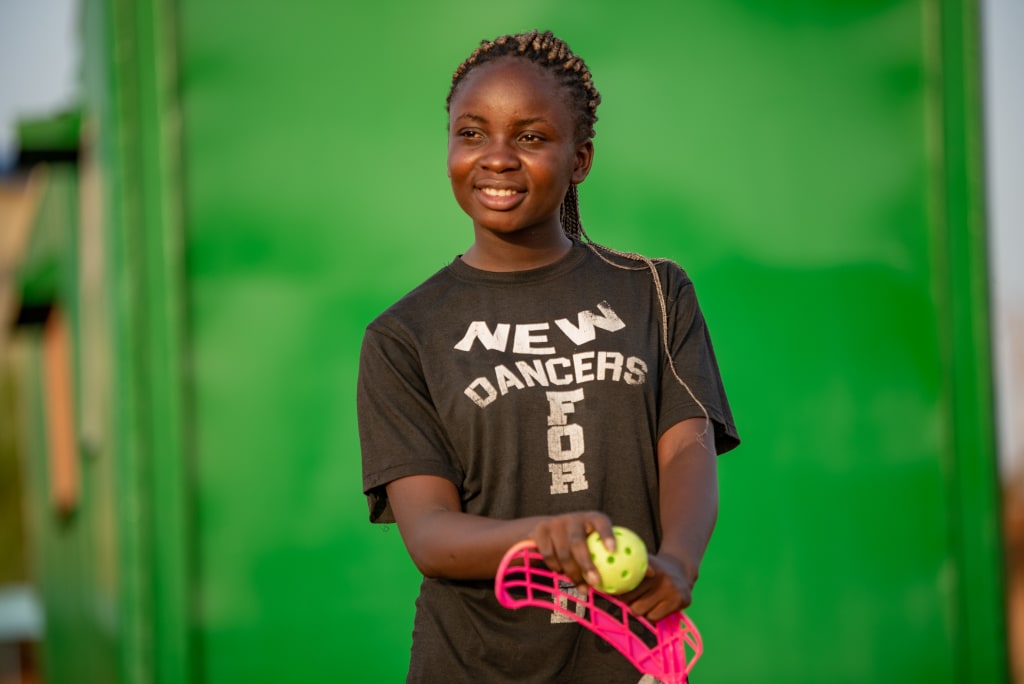 A young girl smiling while holding her floorball equipment.